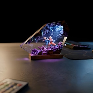 May include: A decorative resin sculpture featuring two figures in combat, set against a backdrop of purple and blue energy effects. The sculpture is encased in a clear, angled frame and mounted on a wooden base, with internal lighting.