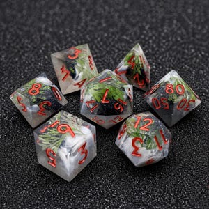 May include: Set of seven polyhedral dice with a clear resin exterior. Each die features a miniature landscape with green foliage, white accents, and red numbering. Ideal for tabletop games and role-playing.