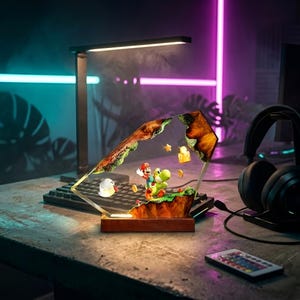 K&ouml;nnte beinhalten: Dekorative Lampe mit einem Videospiel-Diorama mit Mario und Yoshi. Die Lampe hat einen Holzsockel und einen transparenten, geometrischen Rahmen. Eine Schreibtischlampe und Kopfh&ouml;rer sind ebenfalls sichtbar.