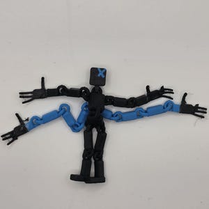 May include: A black articulated action figure with a square head featuring a blue X-shaped face marking. The figure has two black arms and two additional blue chain-link arms extending from the torso, all ending in four-fingered hands.