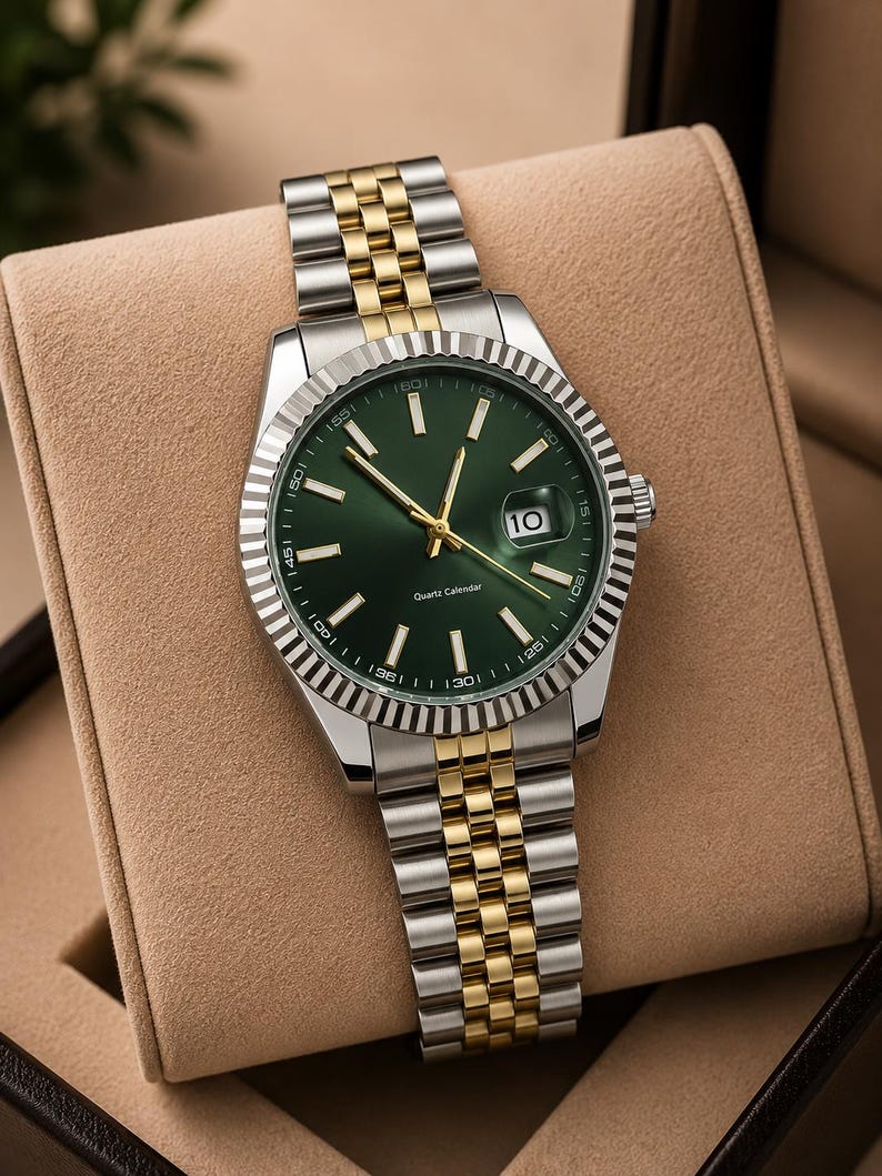 May include: A stainless steel and gold-tone wristwatch with a green dial. The watch features a date display at the 3 o'clock position and a fluted bezel. The watch band is a combination of silver and gold-tone links.