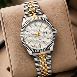 May include: A silver and gold wristwatch with a white dial and a date display at the 3 o'clock position. The watch has a fluted bezel and a two-tone stainless steel and gold-tone link bracelet. The watch is displayed in a tan watch box.