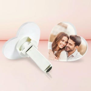 May include: A heart-shaped car air freshener clip featuring a custom photograph of a smiling couple. The white plastic clip mechanism is attached to the back of the heart-shaped frame, designed to secure the item onto a vehicle air vent.