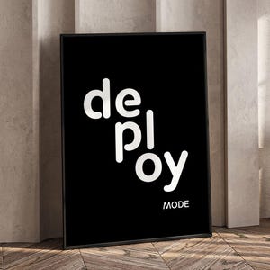 Könnte beinhalten: Ein gerahmter Schwarz-Weiß-Kunstdruck. Der Druck zeigt das Wort "deploy" vertikal in Weiß gestapelt, mit "MODE" in kleinerem weißen Text darunter. Das Kunstwerk wird auf einem Holzboden ausgestellt.
