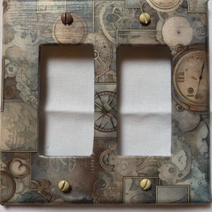 Op de afbeelding: Decoratieve dubbele lichtschakelaar cover met een steampunk design. De cover heeft een collage van klokken, tandwielen en andere mechanische elementen in grijstinten, bruin en beige. De cover is bevestigd met twee bruine en twee crèmekleurige schroeven.