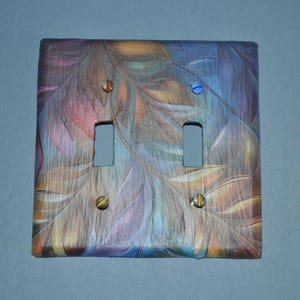 Peut inclure: Un cache-interrupteur double décoratif avec un motif abstrait de plumes aux couleurs violettes, bleues, oranges et jaunes. Le couvercle comporte deux ouvertures pour interrupteurs et est fixé avec quatre vis.