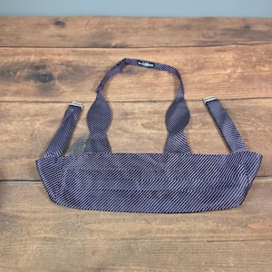 May include: A dark purple cummerbund featuring a subtle diagonal pinstripe pattern. The accessory includes an adjustable strap with a silver-toned metal buckle and a small rectangular brand label attached to the interior neck loop area.