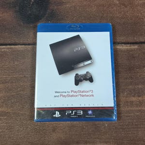 Op de afbeelding: Een blauwe plastic Blu-ray-hoes met een PlayStation 3-speldisc. De hoes toont een zwarte PlayStation 3-console, een zwarte controller en de tekst Welcome to PlayStation 3 and PlayStation Network, met onderaan de tekst Not For Resale.