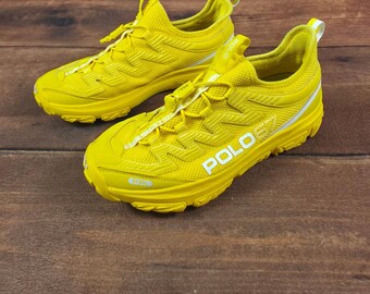 May include: A pair of bright yellow athletic sneakers featuring a mesh upper, a toggle lacing system, and a thick rubber sole. The side of the shoe displays the white text POLO 67, while the tongue and toe area feature additional branding details.