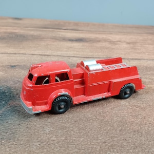 May include: A vintage red toy fire engine with black wheels and silver details. The toy has a ladder on top and a detailed front cab. The fire engine is made of metal and shows signs of wear.
