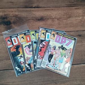 May include: A selection of vintage comic books, featuring the title "DP7" and "New Universe" by Marvel. The covers display colourful illustrations of characters in action, with issue numbers visible. The comics are in protective sleeves, arranged on a wooden surface.