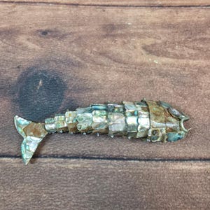 May include: A white ceramic mug with a black handle and the text "But First, Coffee" in a bold, black font. The mug is set against a blurred background, suggesting a cozy setting.