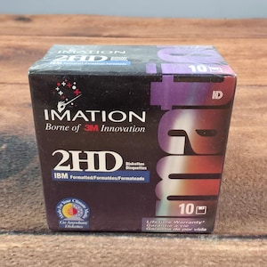 以下が含まれることがあります： IBMフォーマット済みImation 2HDフロッピーディスク10枚入りの未開封ボックス。黒いパッケージにはImationのロゴ、Borne of 3M Innovationの文字、杖を持つ手のグラフィックが描かれています。箱には生涯保証のラベルが含まれています。
