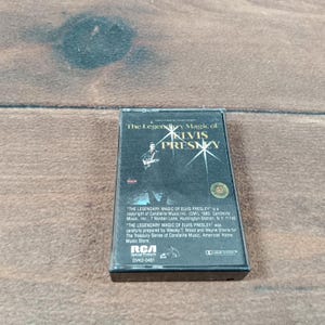 May include: A vintage cassette tape of "The Legendary Magic of Elvis Presley." The cassette has a black and white image of Elvis Presley on the cover. The RCA logo is visible. The text on the cassette includes the title and copyright information.