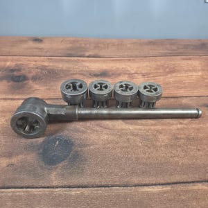 May include: A metal tool with a long handle and a series of circular heads. The tool is made of a dark gray metal and appears to be used for a specific mechanical task. The heads have a cross-shaped design.