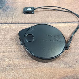 May include: A black Sony AN-51 compact antenna with a black cord and clip. The antenna is round with a small circular button and the Sony logo. The text "AN-51" and "COMPACT ANTENNA" are printed on the antenna.
