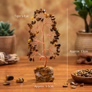 May include: A decorative tree sculpture made of copper wire and tiger's eye gemstones. The tree is approximately 5 inches tall and sits on a stone base. The image also shows loose tiger's eye stones and the text "Tiger's Eye".