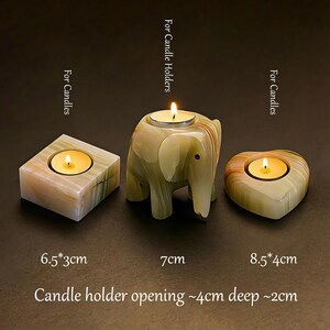 May include: Three stone candle holders with lit candles. The candle holders are a square, an elephant, and a heart shape. The square is 6.5cm x 3cm, the elephant is 7cm, and the heart is 8.5cm x 4cm. The candle holder opening is 4cm deep and 2cm.