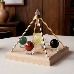 May include: A wooden base with a gold-colored metal pyramid structure. The pyramid holds five gemstone spheres in green, red, yellow, clear, and black. The base has etched designs.