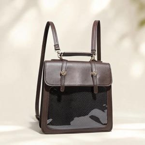 Könnte beinhalten: Ein brauner Lederrucksack mit transparentem Frontpanel und schwarzem Mesh-Innenraum. Der Rucksack hat zwei verstellbare Schultergurte, einen oberen Griff und dekorative Metallbeschläge. Die Tasche ist im Vintage-Stil gestaltet.