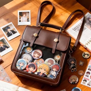 Könnte beinhalten: Braune Kunstleder-Umhängetasche mit transparentem Frontfach, das bunte Anime-Charakter-Anstecknadeln zeigt. Die Tasche hat einen oberen Griff, verstellbare Träger und goldfarbene Hardware. Mehrere kleine Fotos und Aufkleber liegen um die Tasche herum.