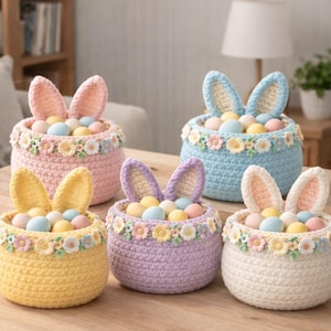 Könnte beinhalten: Fünf gehäkelte Osterkörbe in Pastellfarben: Rosa, Blau, Gelb, Lila und Creme. Jeder Korb hat Hasenohren, einen Blumenschmuck und ist mit bunten Eiern gefüllt. Die Körbe stehen auf einer Holzoberfläche.