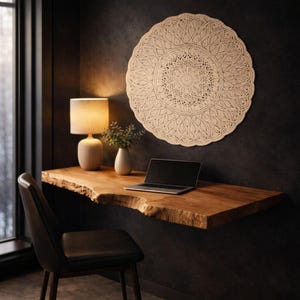 May include: A home office setup featuring a live edge wooden desk with a laptop, a beige lamp, and a black chair. A large, circular, beige, decorative wall hanging is mounted on the dark wall. A small vase with greenery is also on the desk.