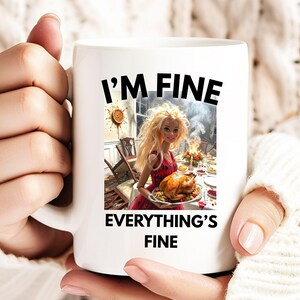 Pode incluir: Caneca de cerâmica branca com o texto "I'M FINE EVERYTHING'S FINE" em preto. A caneca apresenta um gráfico de uma boneca segurando um peru assado em uma mesa com fogo ao fundo. A boneca está usando um vestido vermelho.