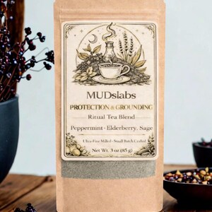 May include: A brown paper bag of MUDslabs Ritual Tea Blend, featuring a detailed label with botanical illustrations and the text "PROTECTION & GROUNDING." The blend includes peppermint, elderberry, and sage. Net weight is 3 oz (85 g).