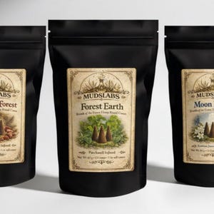 May include: Three black pouches with labels reading "MUDSLABS." Each label is labelled with a different name: "Blood of the Forest," "Forest Earth," and "Moon Bloom." The labels feature illustrations of cones and botanical elements.