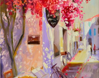 Può includere: Un dipinto che rappresenta una scena di strada con un edificio rosa e un albero con fiori rossi. C'è un tavolo con due sedie e una bicicletta appoggiata al muro. La strada è pavimentata con pietre rosse e bianche.