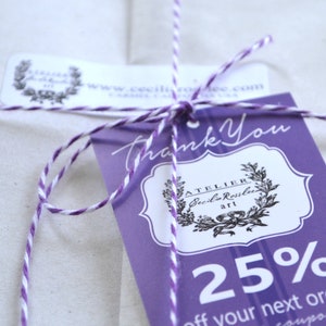May include: A close-up of a gift tag tied with purple and white twine. The tag is purple with white text that says "Thank You" and features a logo and the text "ATELIER Cecilia Rosslee art". The tag also includes the text "25% off your next order".