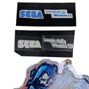 May include: Several SEGA logo stickers, some with "Compatible with Microsoft Windows CE" text. The bottom image shows a holographic design with a blue grim reaper and the text "GAMER GHOSTS".