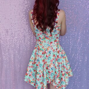 May include: A woman wearing a light blue dress with a floral print. The dress has a high neckline and a short, asymmetrical hemline. The dress is made of a lightweight fabric and has a relaxed fit.
