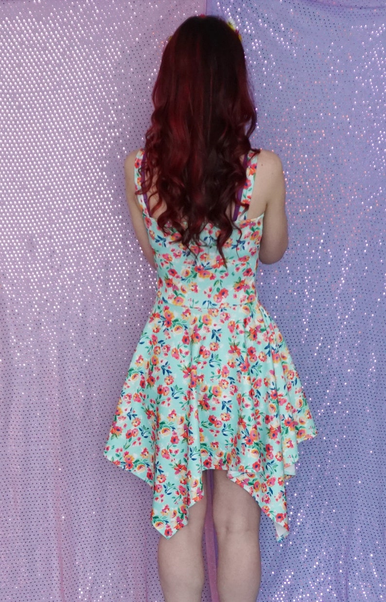 May include: A woman wearing a light blue dress with a floral print. The dress has a high neckline and a short, asymmetrical hemline. The dress is made of a lightweight fabric and has a relaxed fit.