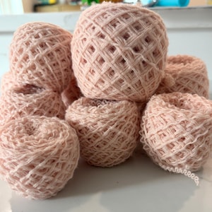 May include: A collection of light pink yarn balls. The yarn is loosely woven, creating a textured appearance. The balls vary in size and are stacked together, showcasing the soft, pastel color and the potential for crafting projects.