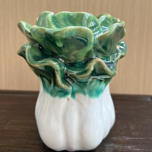 Może przedstawiać: Ceramiczny wazon w kształcie główki kapusty bok choy lub kapusty pekińskiej. Podstawa jest gładka, błyszcząca i biała, przechodząca w pofalowane, warstwowe liście w odcieniach głębokiej leśnej zieleni i szmaragdu, z wykończeniem na wysoki połysk.