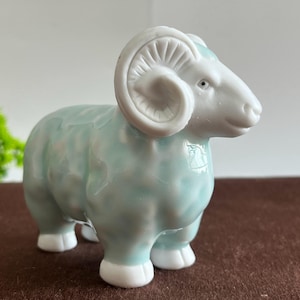 May include: A ceramic ram figurine in a light blue and white colour scheme. The ram has large, curved horns and is standing on four white feet. The figurine has a glossy finish and is a decorative item.