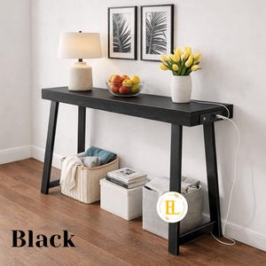 May include: Black console table with a rectangular top and angled legs. The table has a built-in power outlet and is decorated with a lamp, fruit, and flowers. The word "Black" is printed at the bottom.