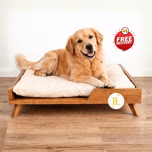 May include: A golden retriever dog rests on a wooden dog bed with a cream-colored cushion. The bed has a rectangular frame and angled legs. The dog is smiling, and the bed is on a wood floor.