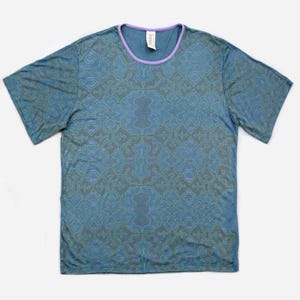 May include: A blue short-sleeved t-shirt with a purple trim around the neckline. The shirt has a repeating pattern of green and purple geometric shapes.