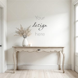 May include: A light-colored wooden console table with a scalloped edge, a white vase with dried flowers, and a lit candle. The wall behind the table has the text "Your design here". The room has a neutral color palette.