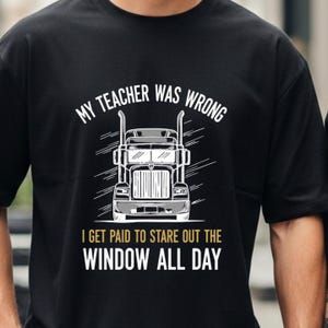 May include: Black t-shirt with a white and gray graphic of a semi-truck. The text above the truck reads "MY TEACHER WAS WRONG." Below the truck, the text says "I GET PAID TO STARE OUT THE WINDOW ALL DAY."