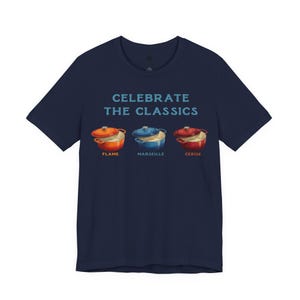 Navy crew-neck t-shirt reads, "CELEBRATE THE CLASSICS" with three dutch ovens, in colors Flame, Marseille, and Cerise.