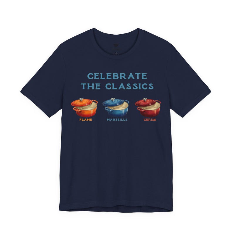 Navy crew-neck t-shirt reads, "CELEBRATE THE CLASSICS" with three dutch ovens, in colors Flame, Marseille, and Cerise.