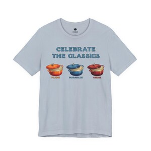 Light blue-gray crew-neck t-shirt reads, "CELEBRATE THE CLASSICS" with three dutch ovens, in colors Flame, Marseille, and Cerise.
