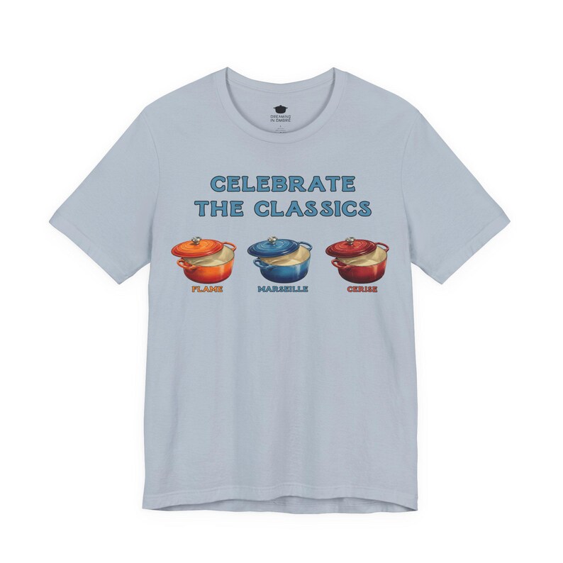 Light blue-gray crew-neck t-shirt reads, "CELEBRATE THE CLASSICS" with three dutch ovens, in colors Flame, Marseille, and Cerise.
