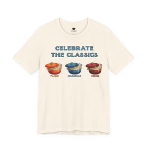 Cream colored crew-neck t-shirt reads, "CELEBRATE THE CLASSICS" with three dutch ovens, in colors Flame, Marseille, and Cerise.