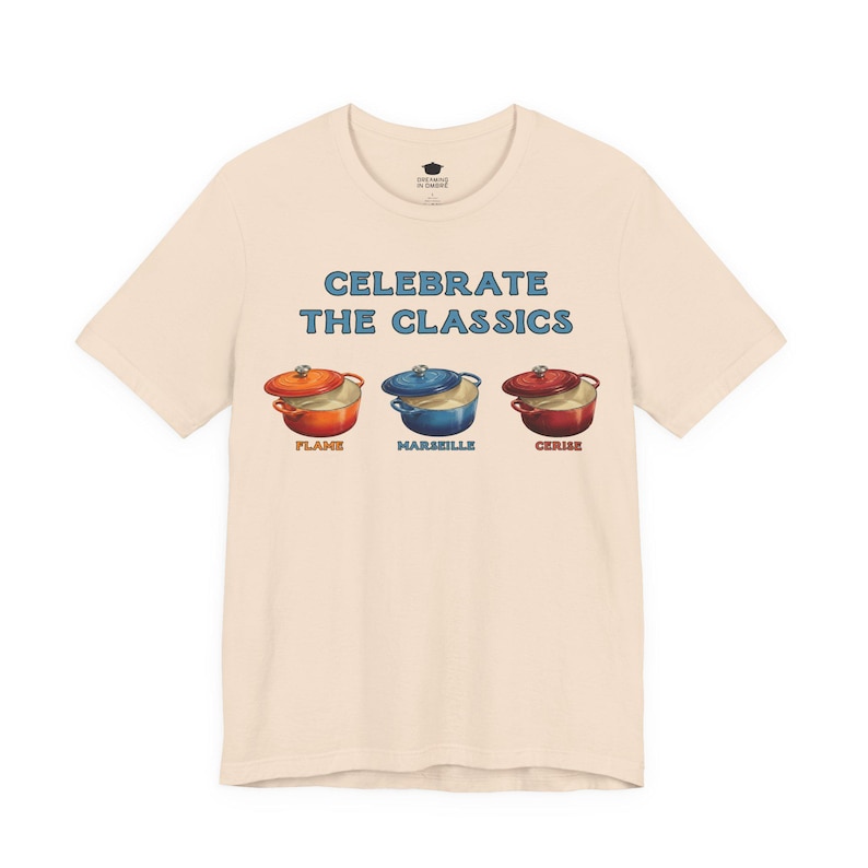 Cream colored crew-neck t-shirt reads, "CELEBRATE THE CLASSICS" with three dutch ovens, in colors Flame, Marseille, and Cerise.