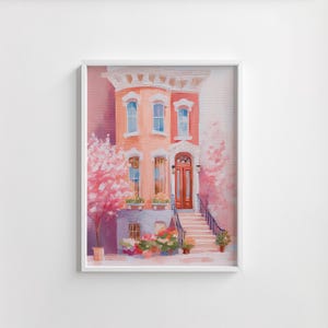 Puede incluir: Pintura de acuarela enmarcada de una casa con fachada rosa y melocotón. La casa tiene varias ventanas, una puerta roja y una escalera que conduce a la entrada. Los árboles en flor rosas y los maceteros añaden color.